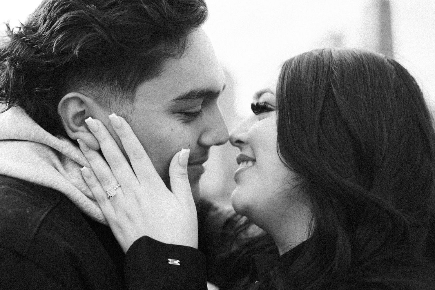 Black and white close-up of a couple nearly kissing, engagement ring visible on her hand.