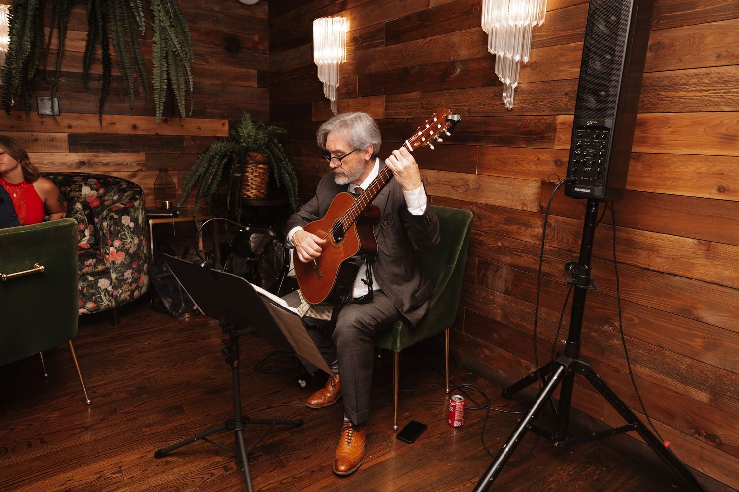 Guitarist in suit performing classical music for wedding guests in warmly lit rustic wood-paneled room.