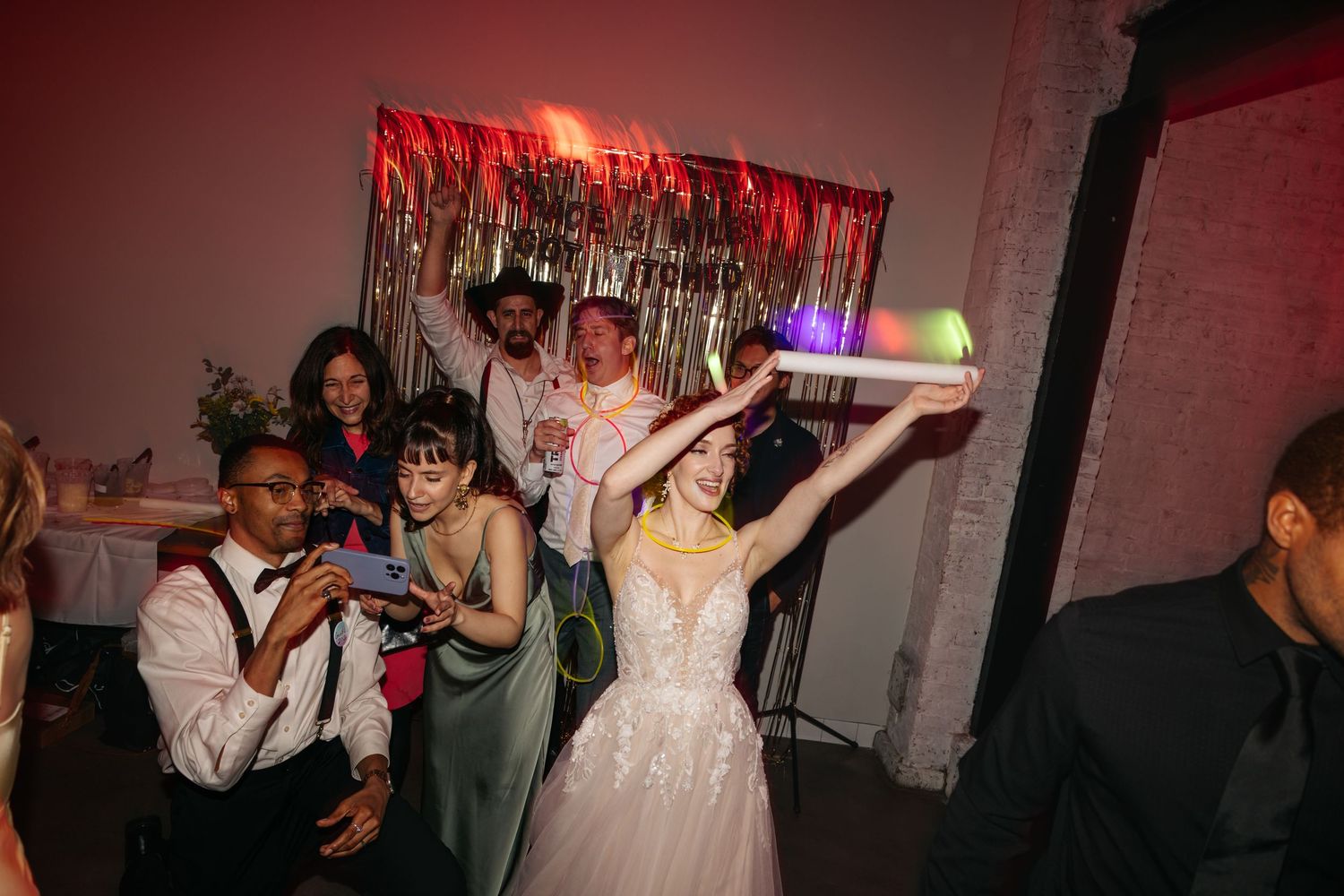 Bride in white gown dances joyfully with guests at a vibrant wedding reception party.