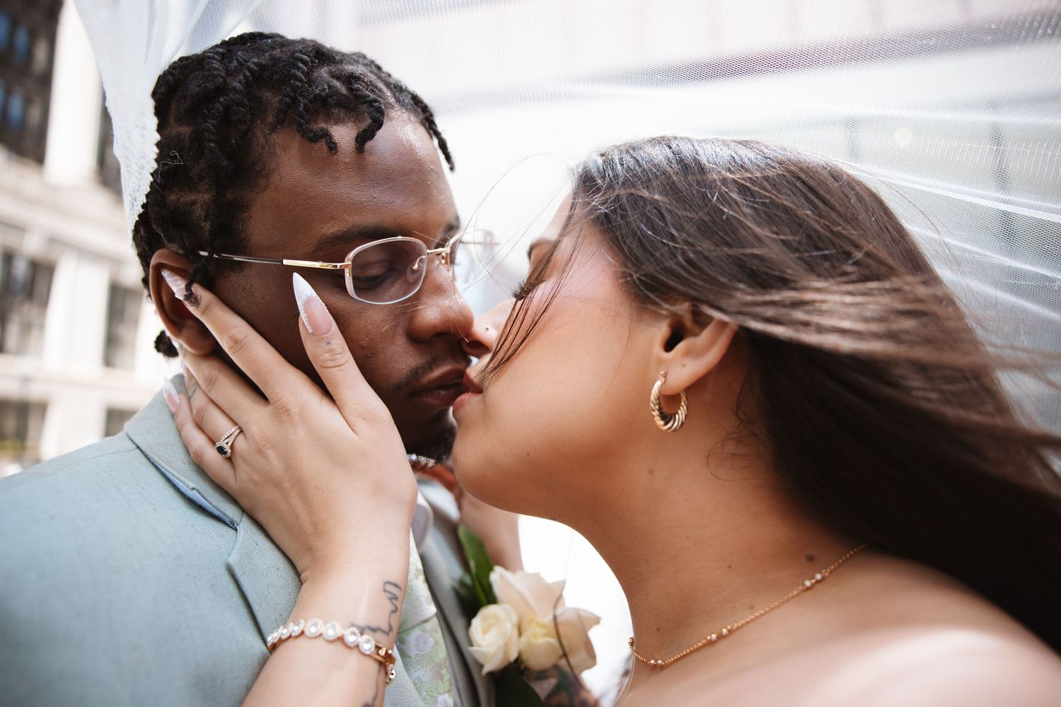 Interracial couple sharing intimate kiss under bridal veil on wedding day.