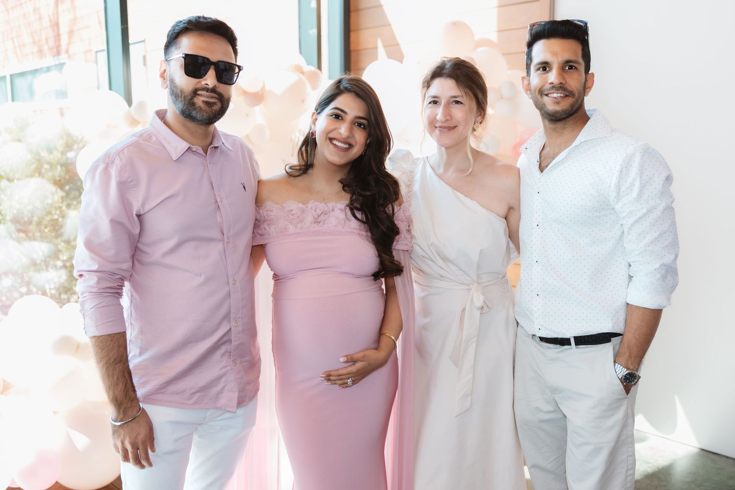 Two couples pose at baby shower, featuring pregnant woman in pink off-shoulder dress.