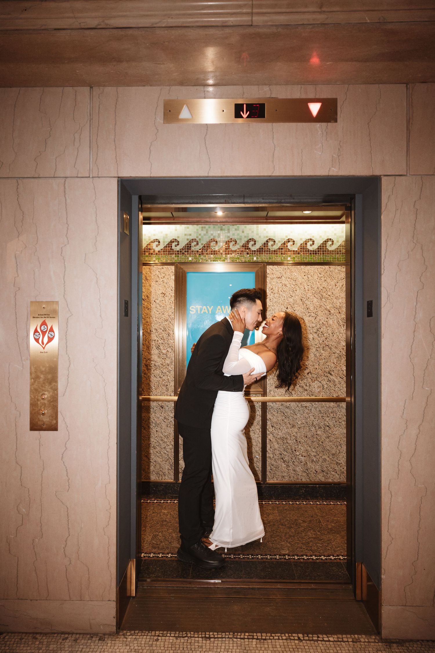 Newlyweds sharing a passionate kiss inside a decorated elevator with ornate surroundings.