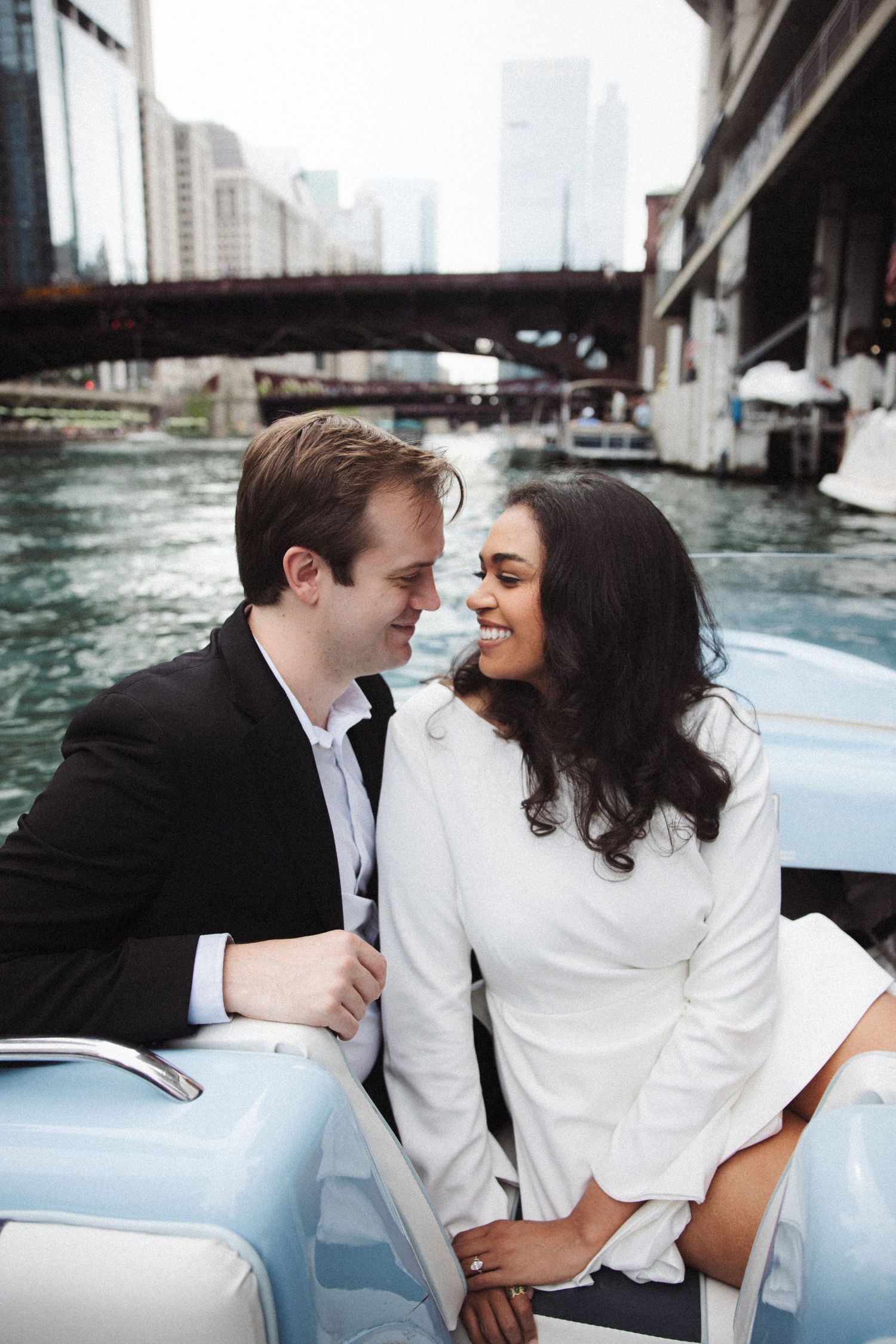 Couple sharing a romantic moment on a blue boat along the Chicago River with city bridges in the background.