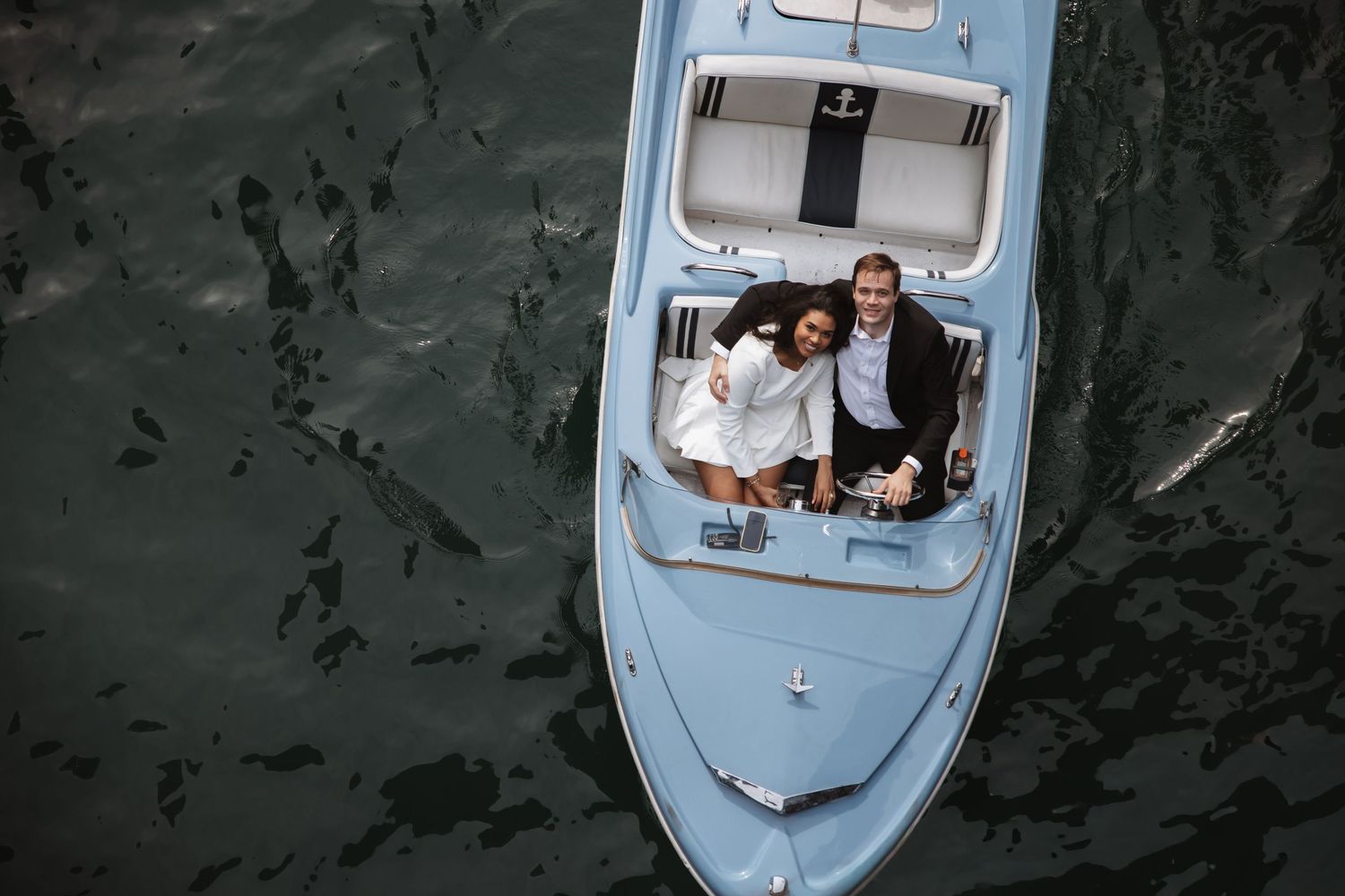 Aerial view of a couple smiling together on a light blue luxury yacht surrounded by dark water.