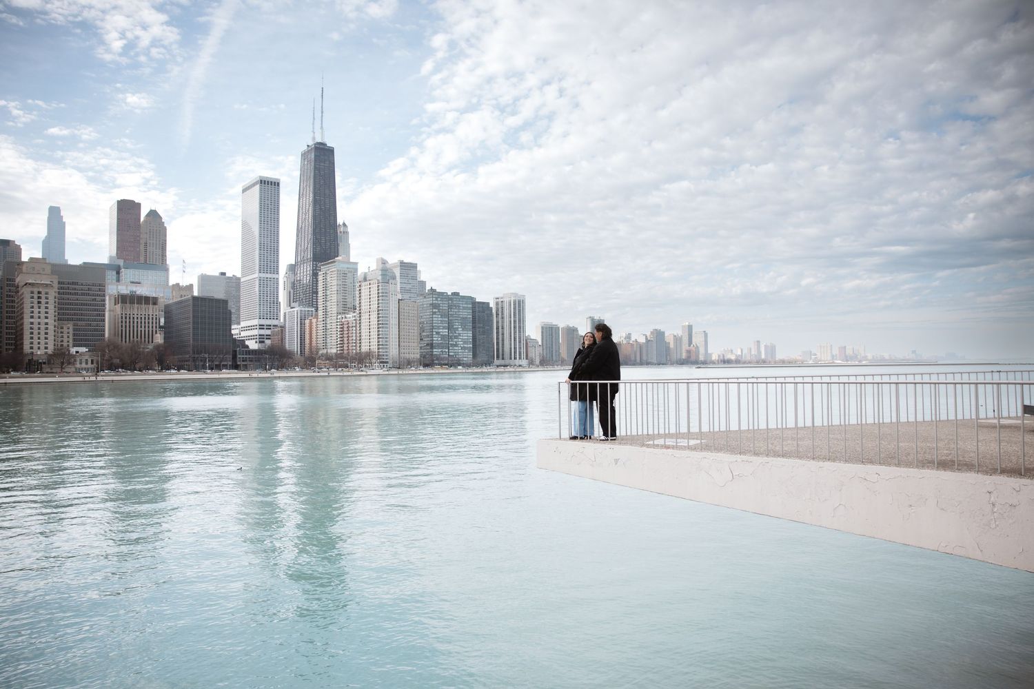 Couple standing together on a lakefront pier admiring the expansive Chicago skyline on a cloudy day.