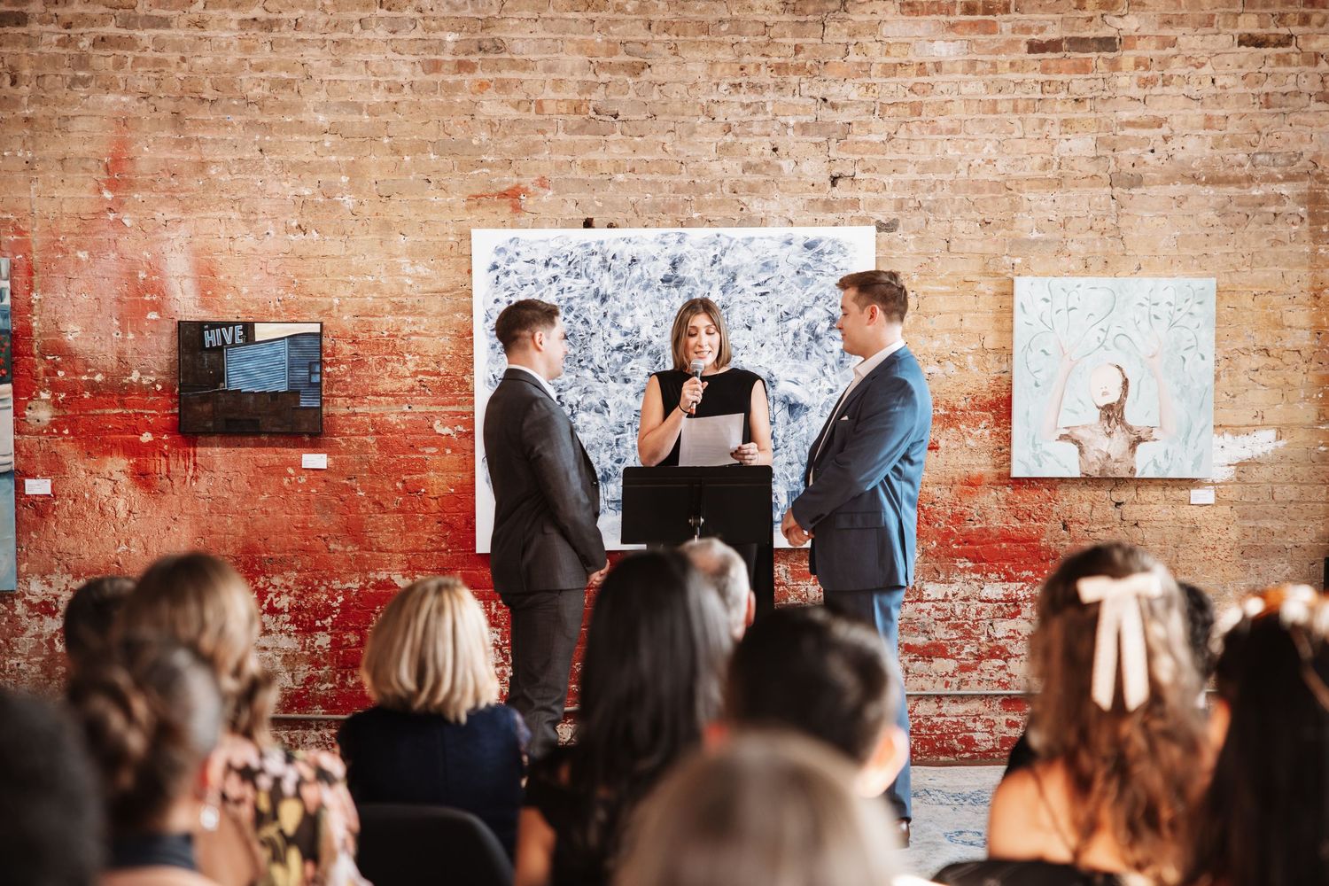 Wedding ceremony with officiant reading vows to couple before brick wall gallery.