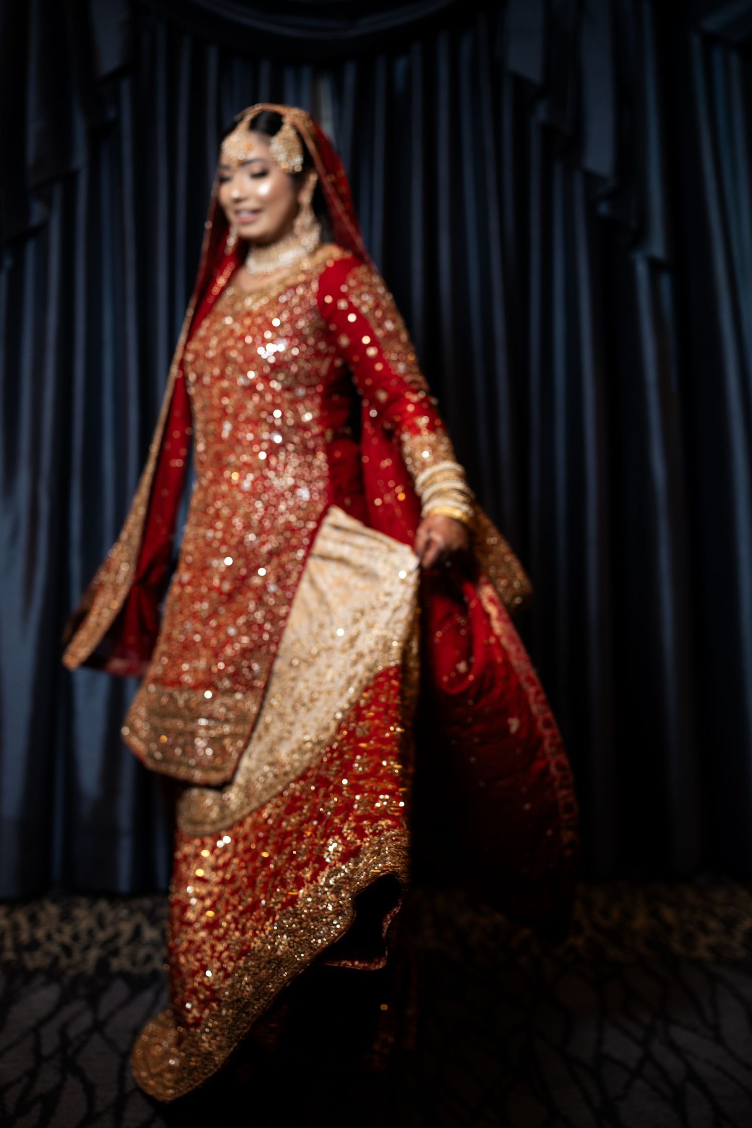 South Asian bride posing in elaborate red and gold embroidered lehenga with bridal jewelry and dupatta.