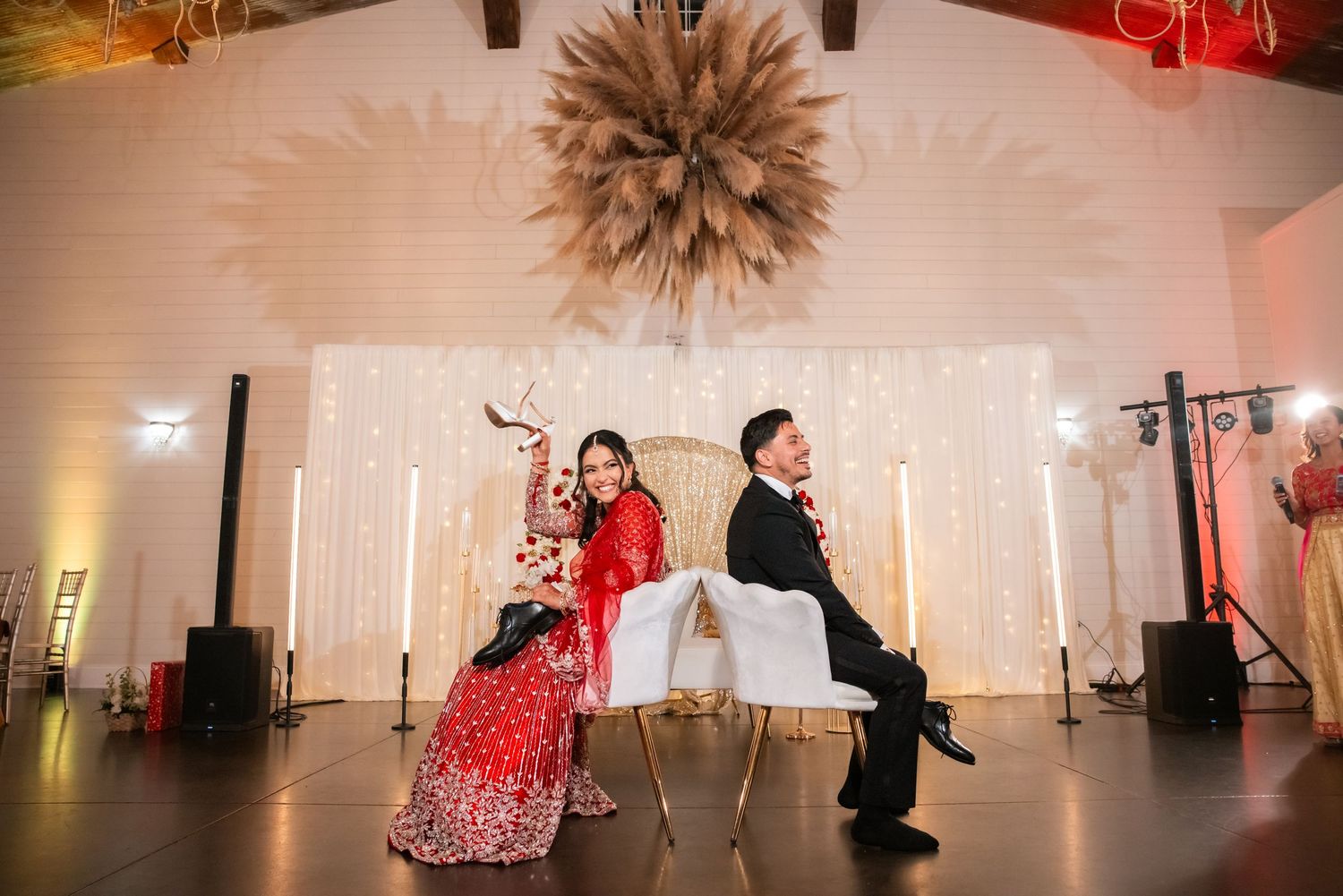 Bride in red lehenga and groom in tuxedo posing at wedding reception.