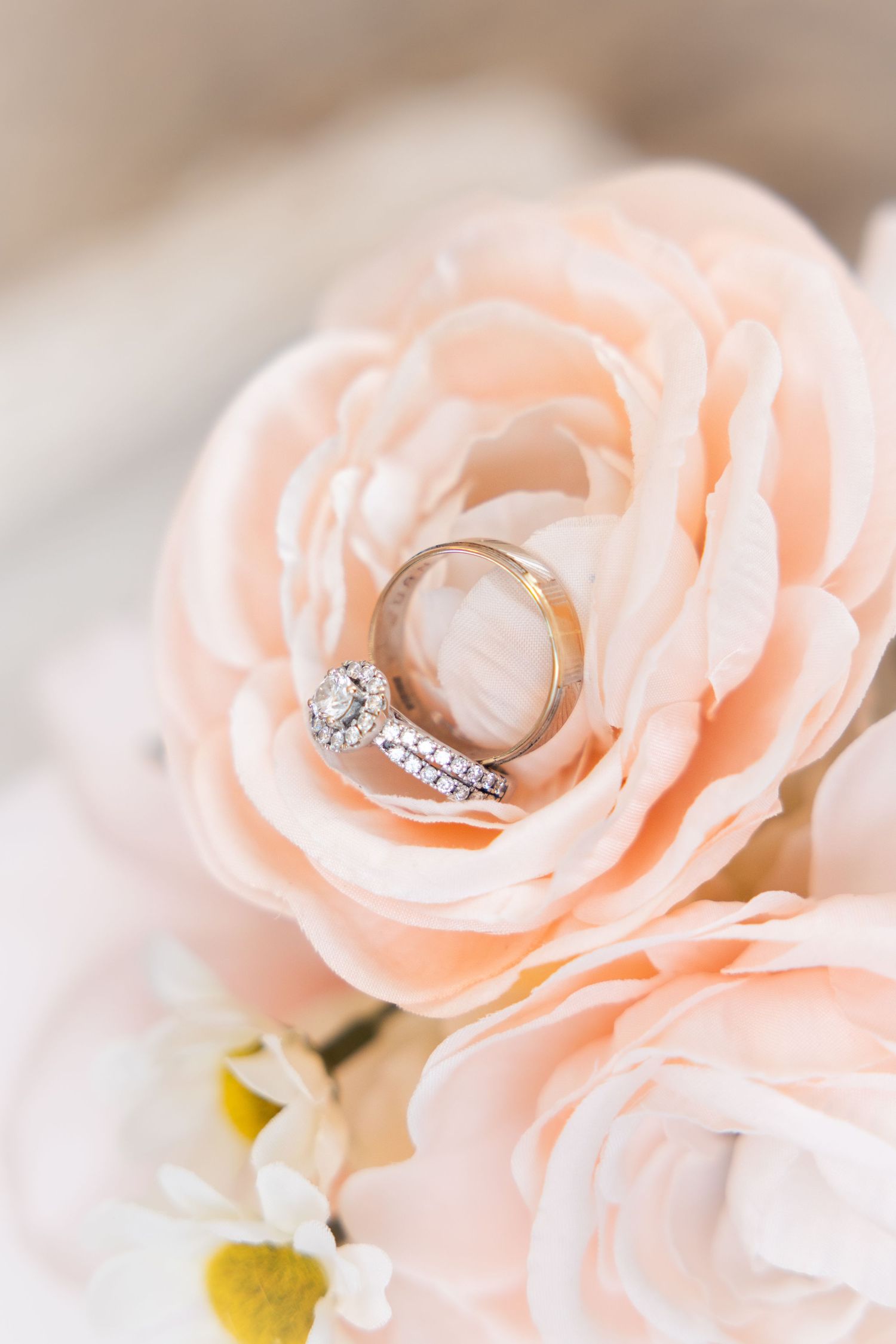 Diamond engagement ring and gold wedding band nestled in blush ranunculus flower.