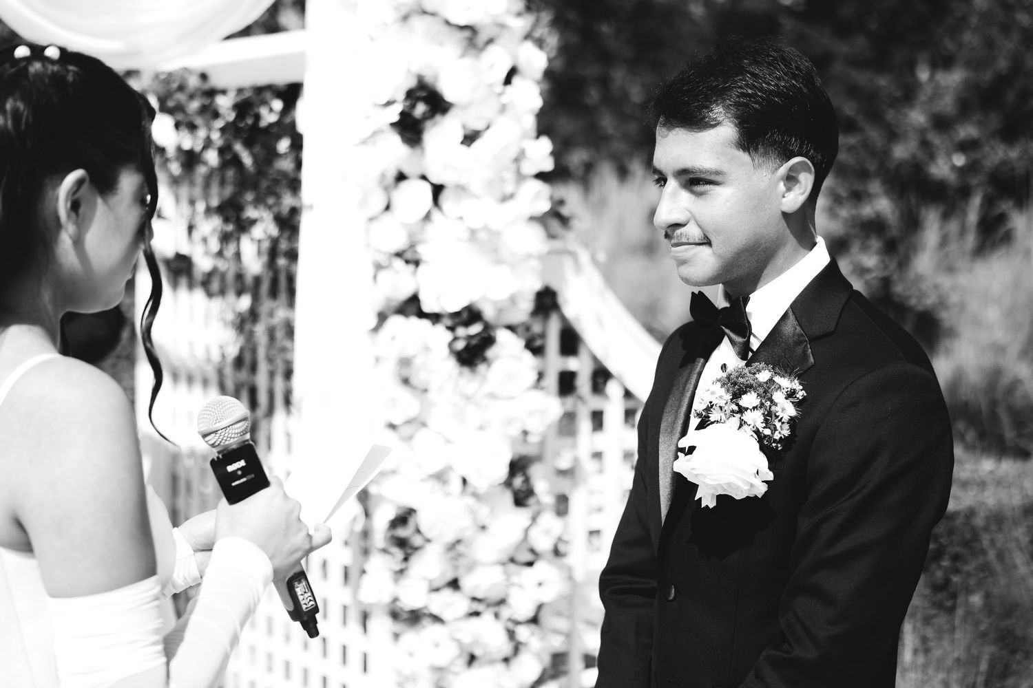 Groom tenderly touches brides face during emotional outdoor wedding ceremony in black and white.