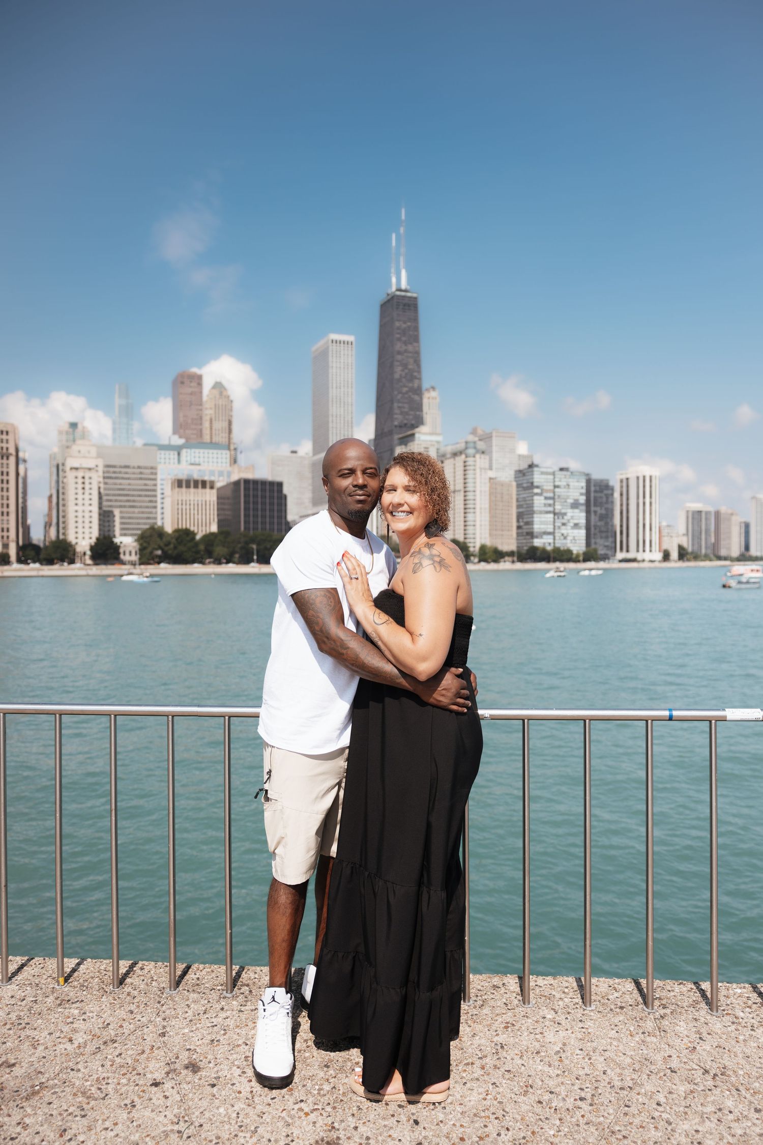 Couple embracing and smiling with Chicago skyline and Lake Michigan visible behind them on a bright sunny day.