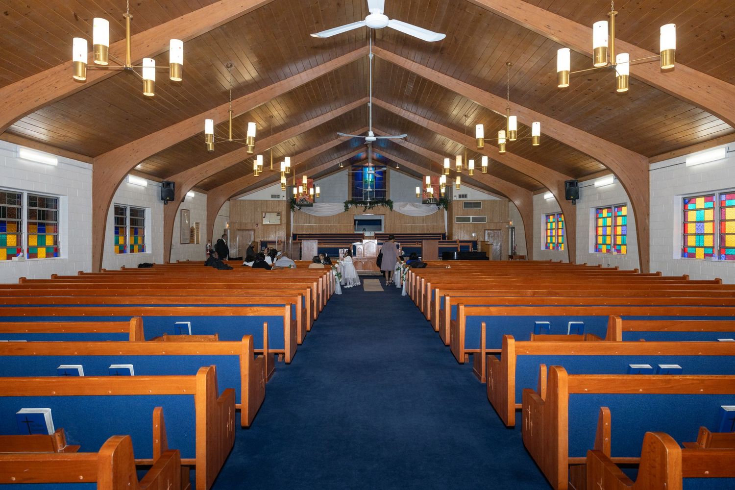 Interior of a church with wooden pews, blue carpet, stained glass windows, and vaulted ceiling.