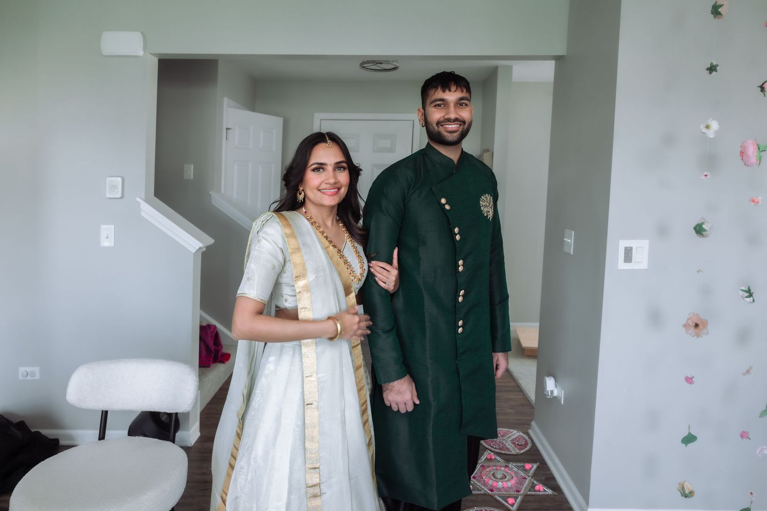 Indian couple poses together in traditional attire, bride in white lehenga and groom in green sherwani.