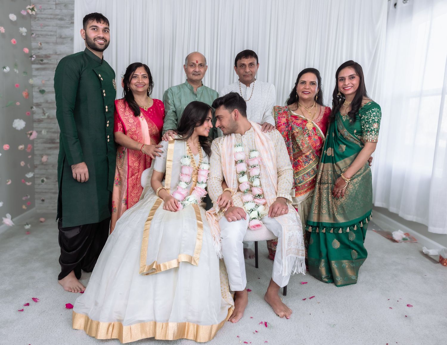 Indian wedding family portrait with bride in white lehenga and groom in sherwani surrounded by relatives in traditional attire.