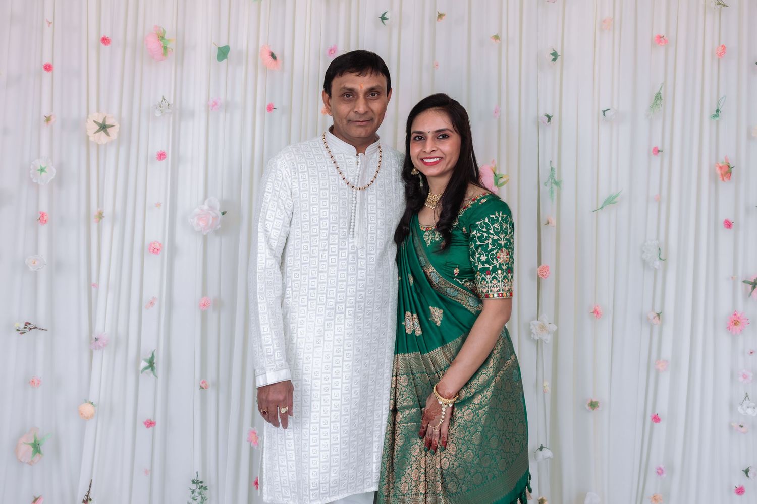 Indian couple smiling together, man wearing white kurta pajama and woman in elegant green Banarasi saree at an event.