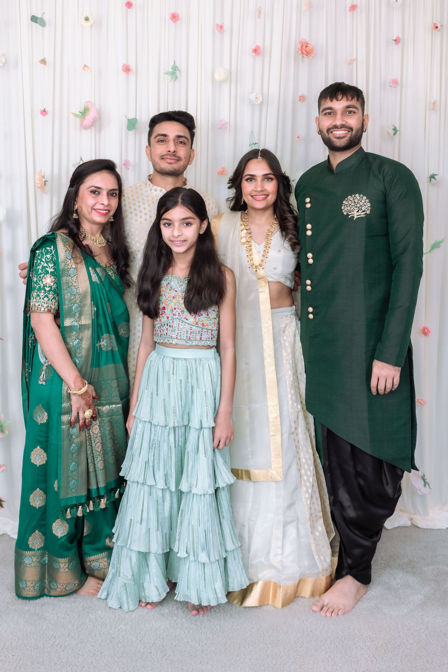 Indian family of five in traditional green and white outfits pose at a festive celebration backdrop.