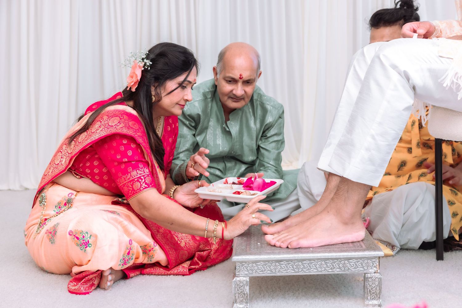 Indian bride in red saree performs traditional foot washing ritual with elder during Hindu wedding.