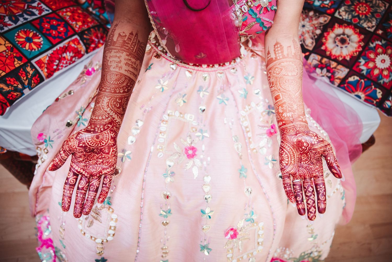 Bride's hands showing detailed henna mehndi artwork displayed over floral pink lehenga.