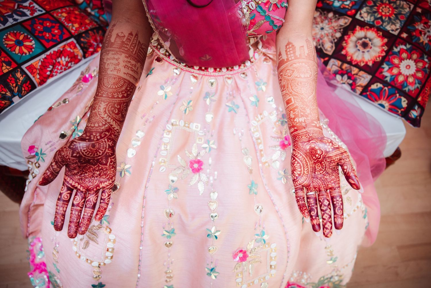 Bride displaying intricate henna mehndi designs on both hands over floral pink lehenga.