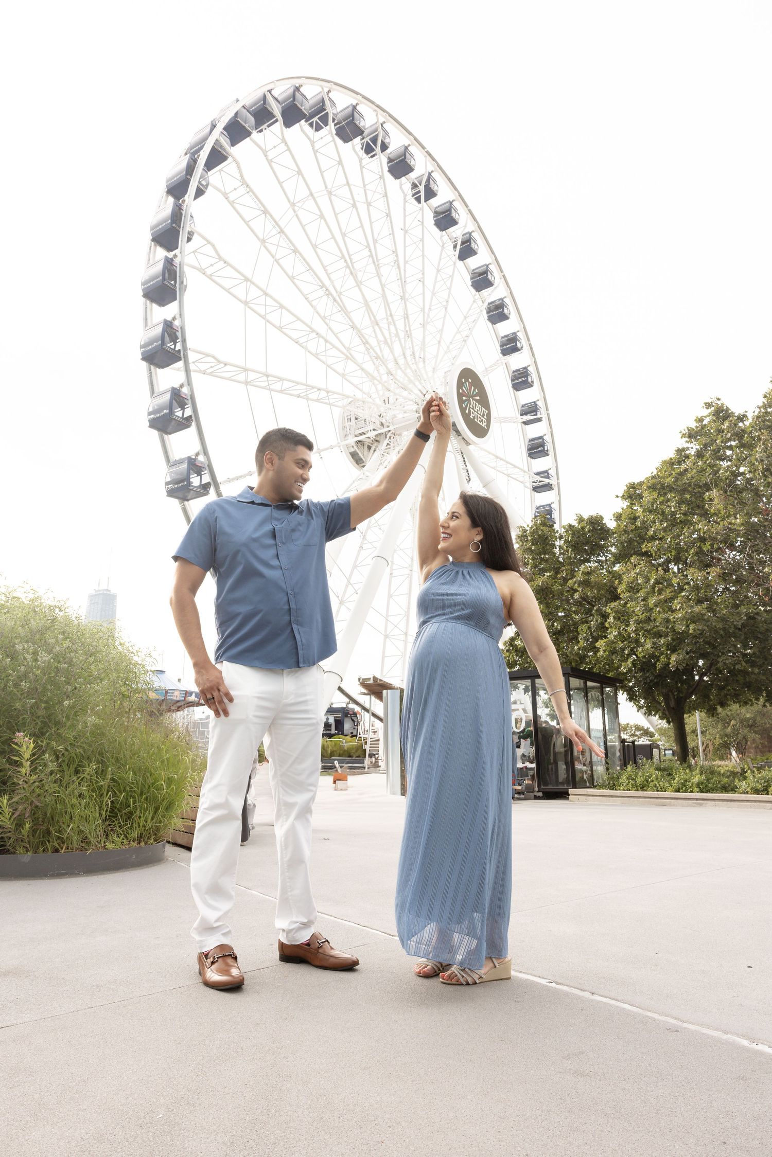 Couple holding hands and dancing near a ferris wheel, pregnant woman in flowing blue gown.