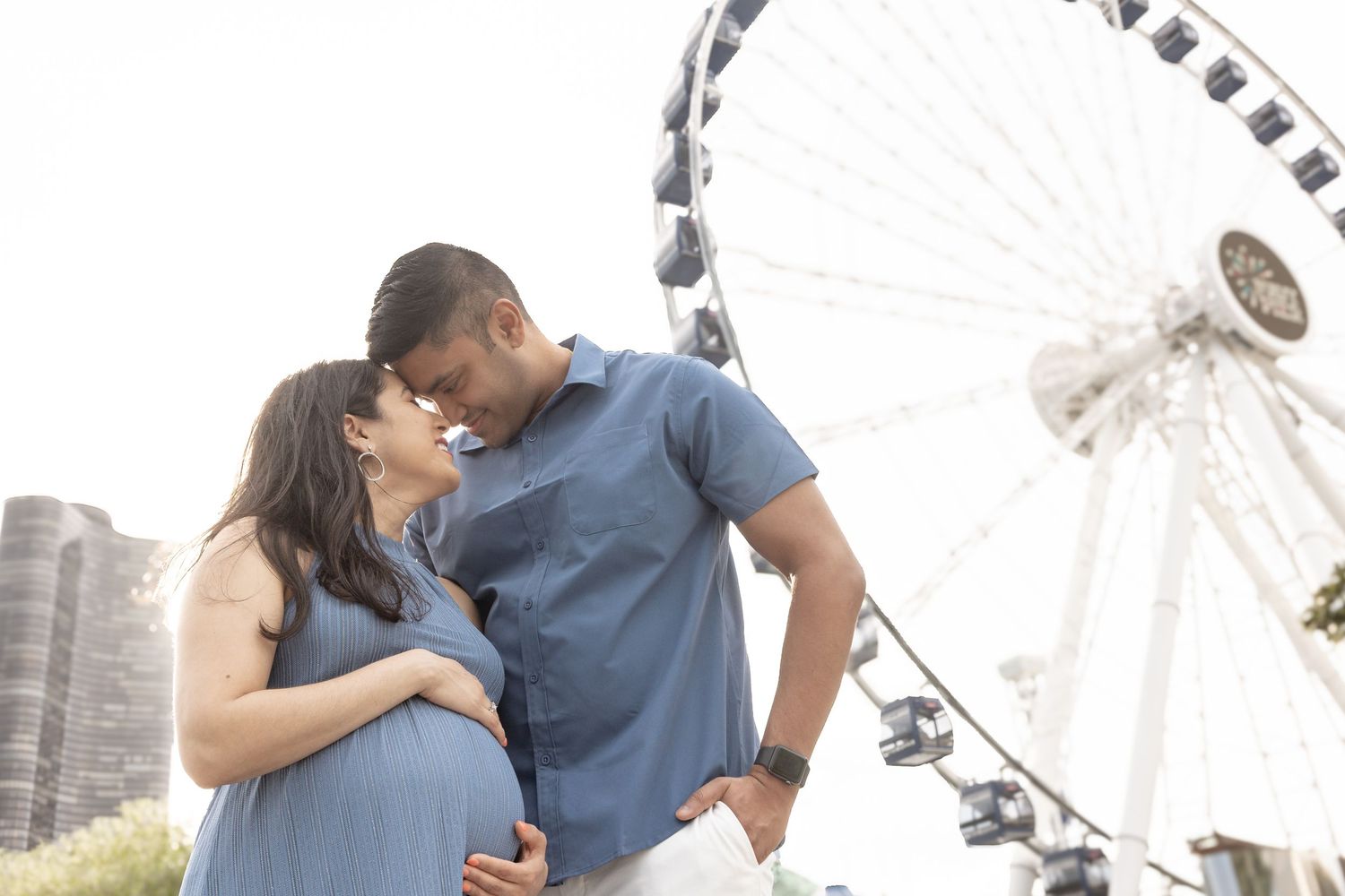 Couple sharing tender moment near Ferris wheel during maternity shoot.