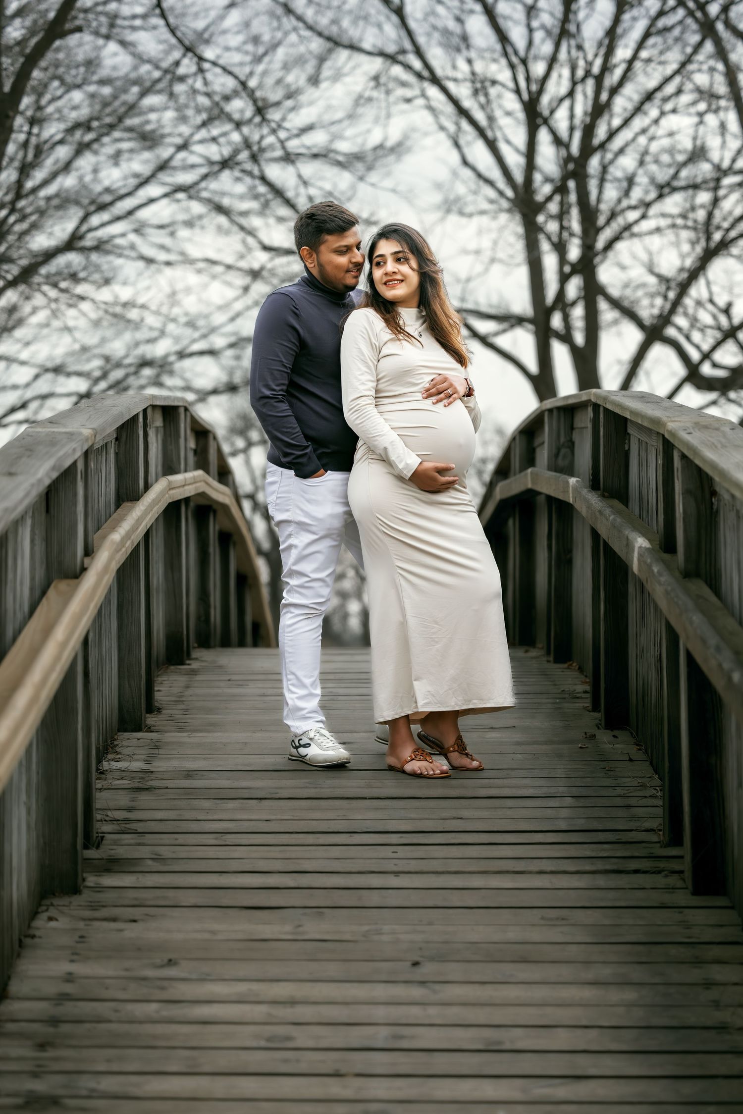 Expecting couple embracing on wooden bridge during maternity photoshoot in autumn park.