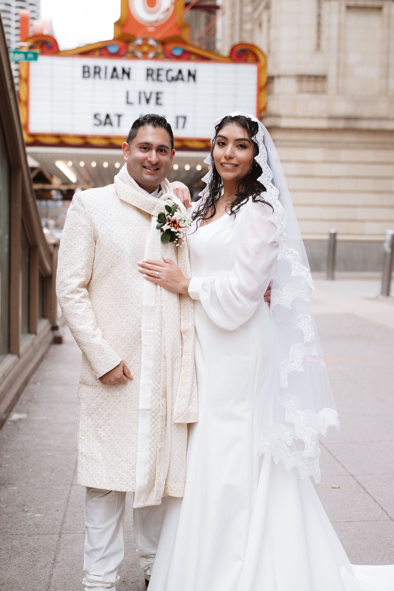 Bride and groom in white wedding attire pose outside Chicago Theatre marquee on their wedding day.