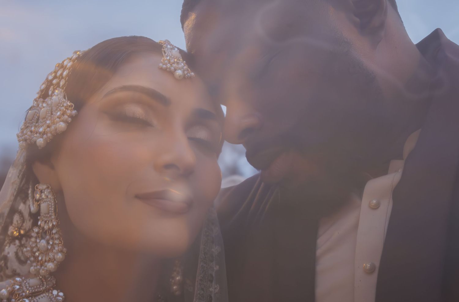 Intimate close-up of South Asian bride and groom touching foreheads tenderly during wedding ceremony.