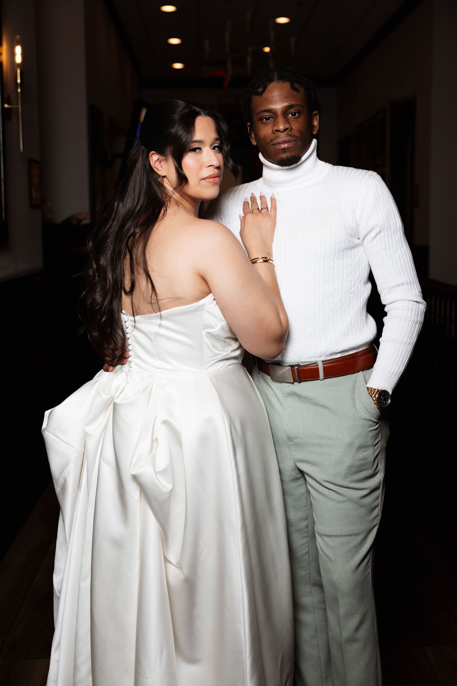 Bride in white strapless ball gown and groom in white turtleneck posing at wedding reception.