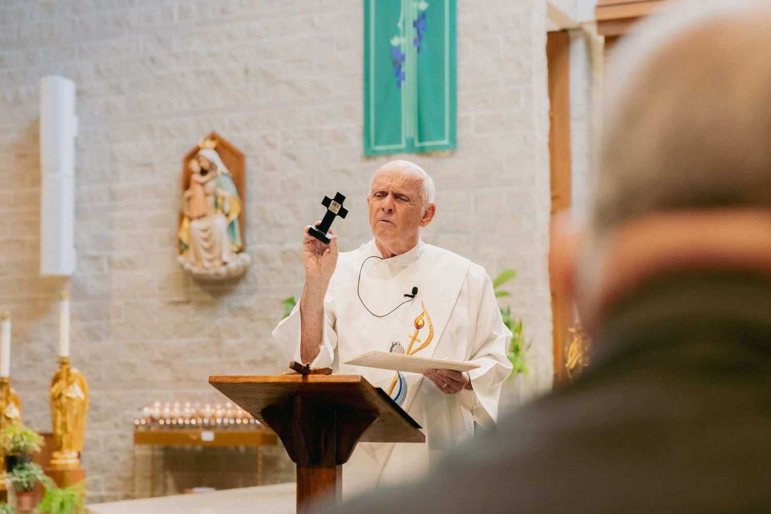 Priest holding a cross while delivering a sermon at a church altar during a religious ceremony.