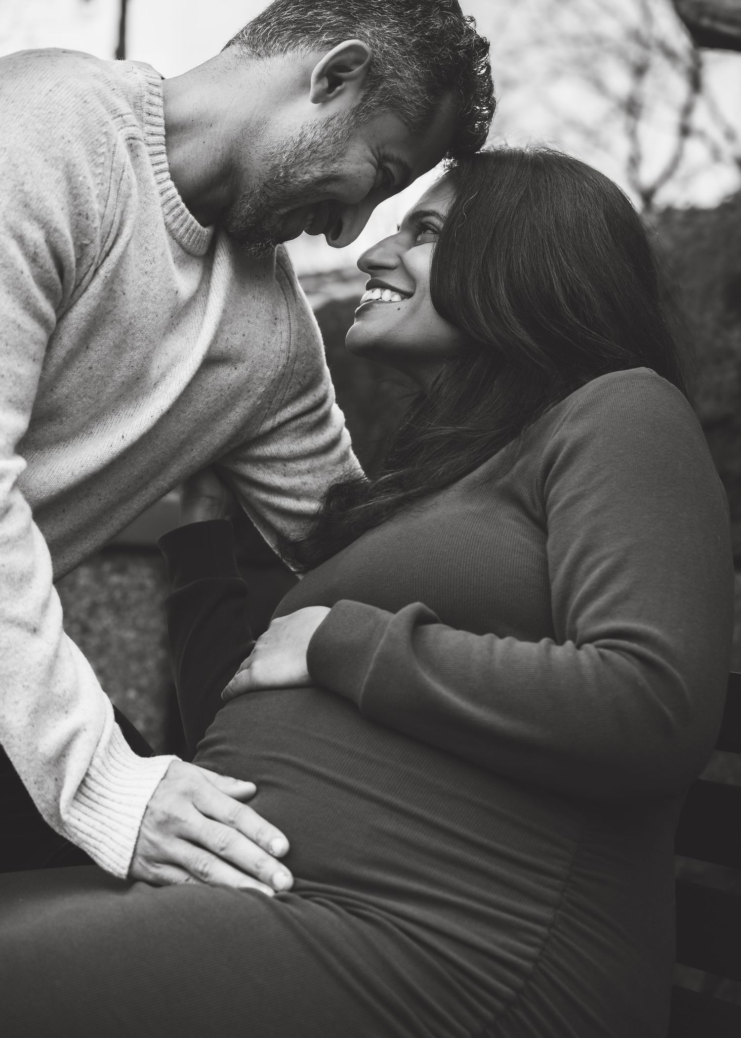 Black and white photo of a couple sharing a tender moment, man touching pregnant woman's belly outdoors.