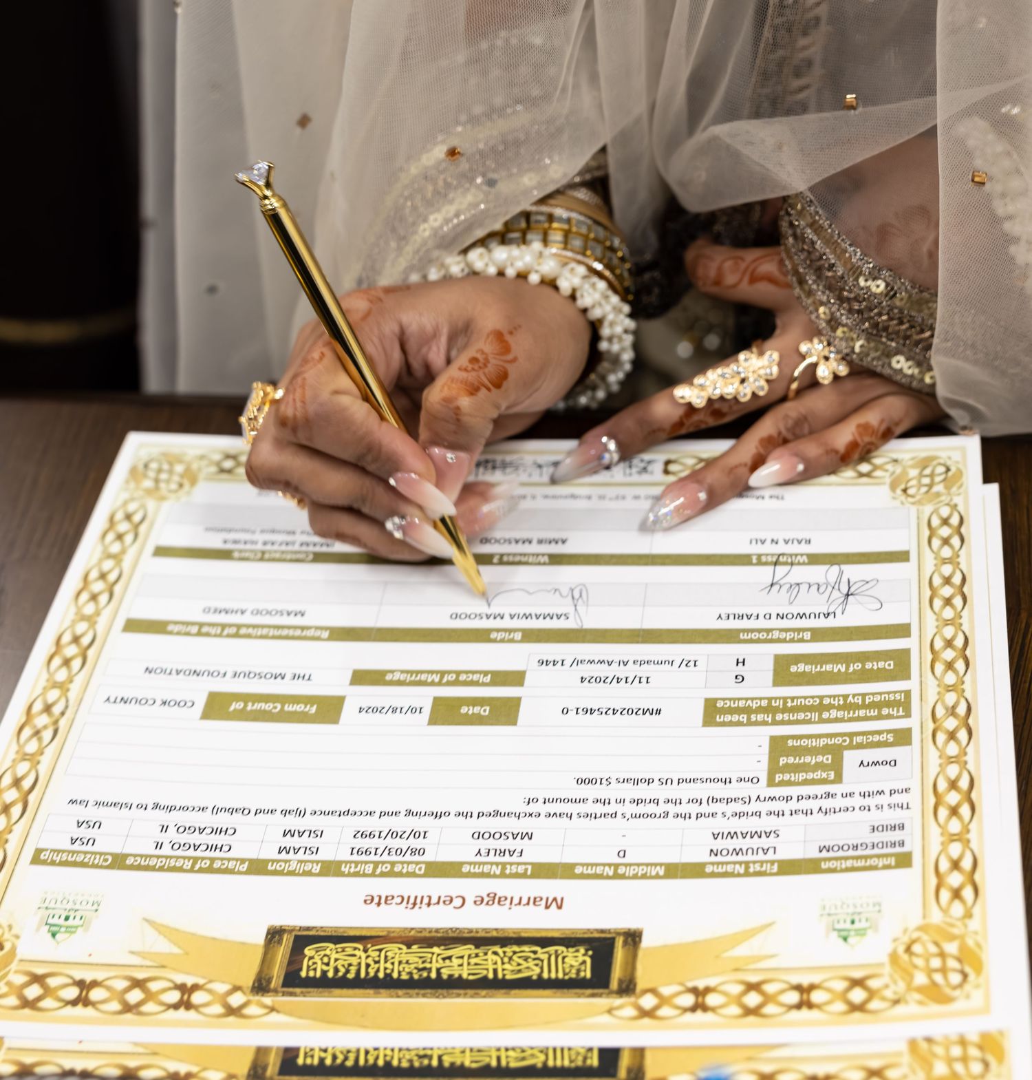 Bride with henna hands and gold jewelry signing Islamic marriage certificate in ornate wedding attire.