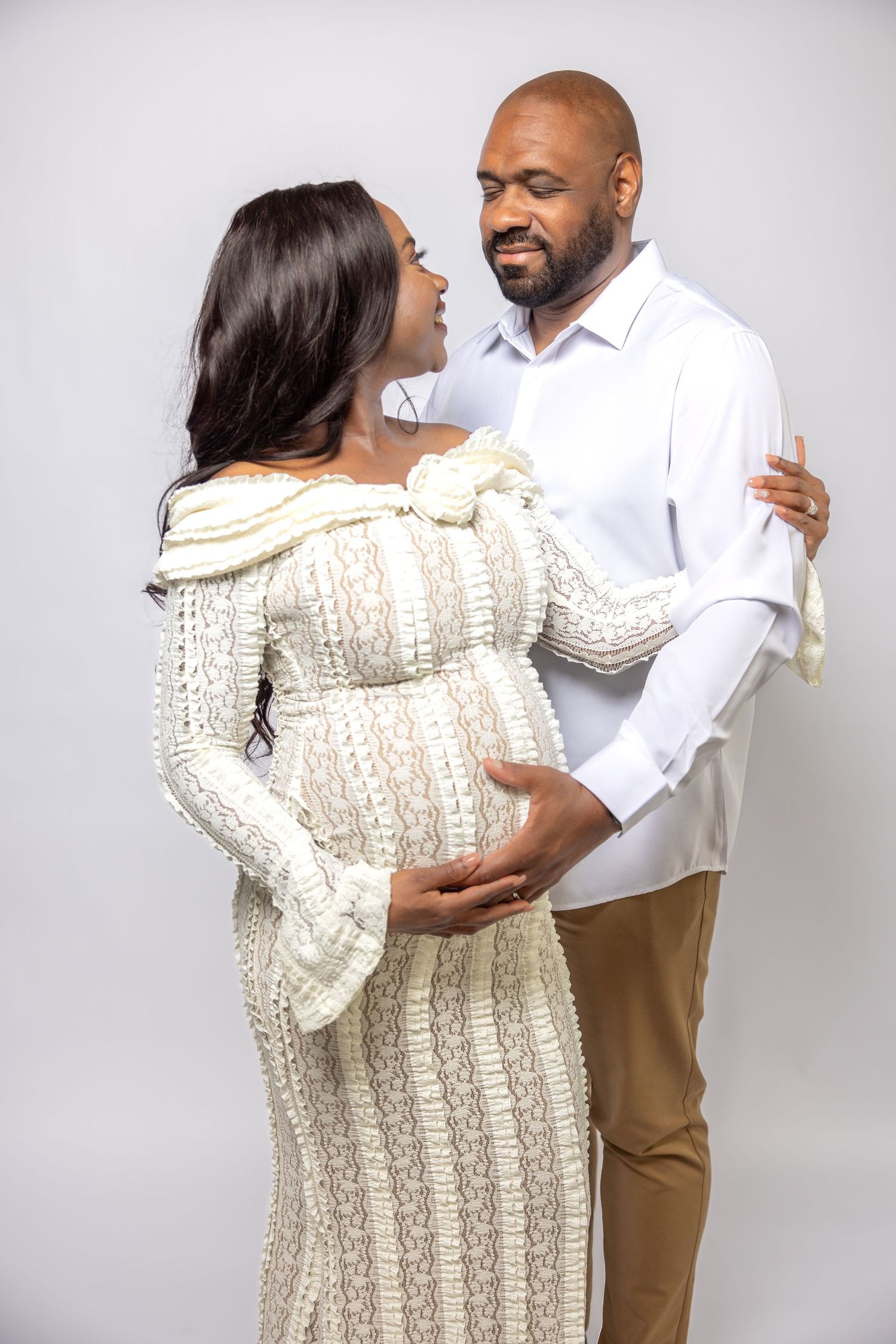 Couple sharing tender moment during maternity shoot, man in white shirt holding pregnant partners belly.