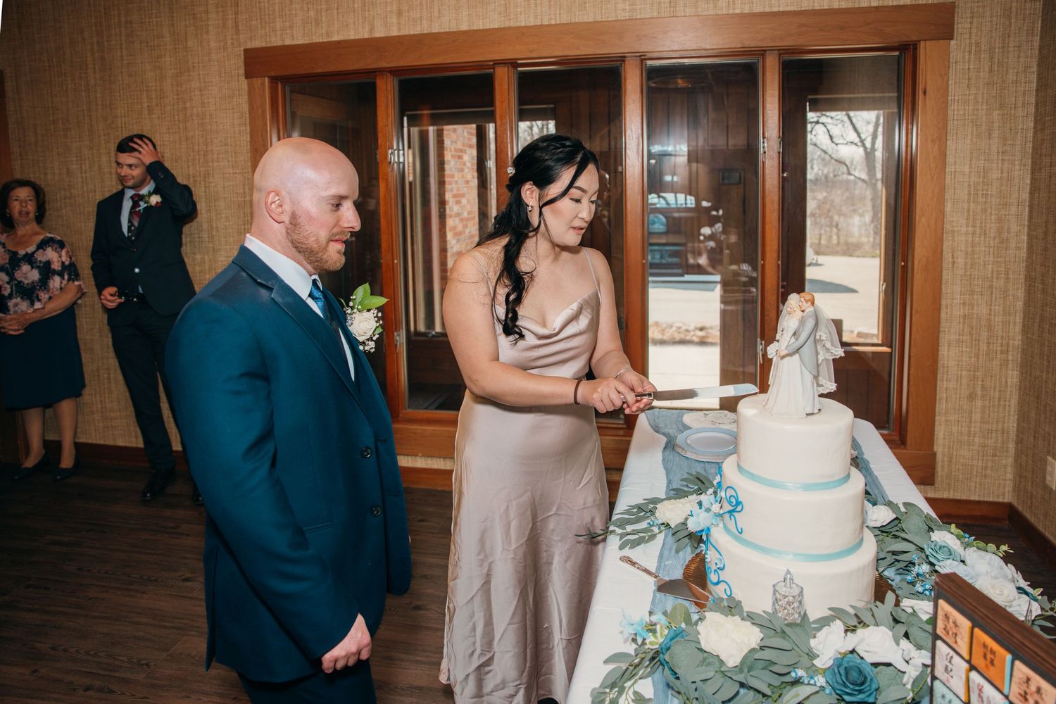 Bride and groom preparing to cut their blue and white three-tier wedding cake at reception.
