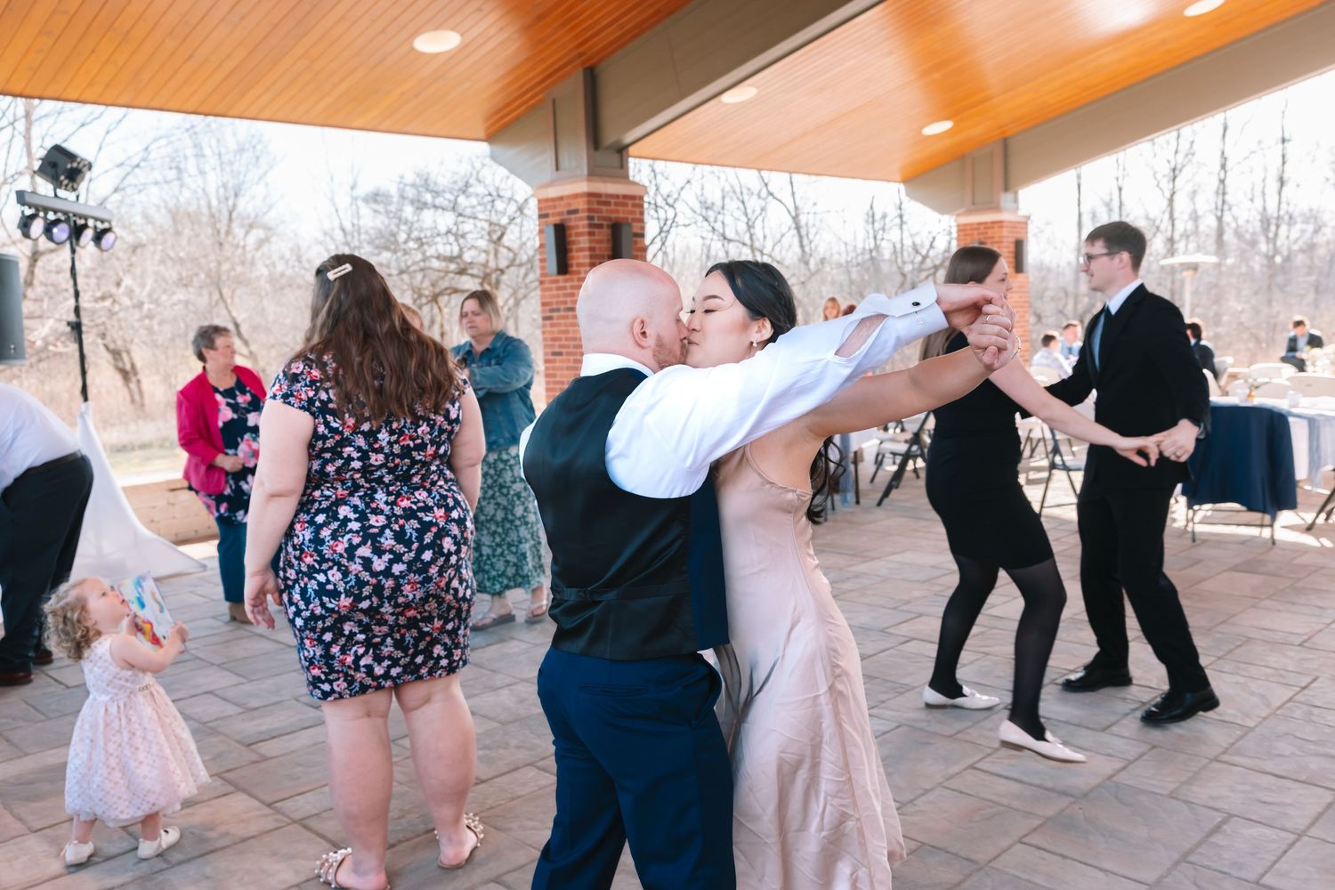 Bride and groom share a kiss on the dance floor surrounded by wedding guests at outdoor reception.