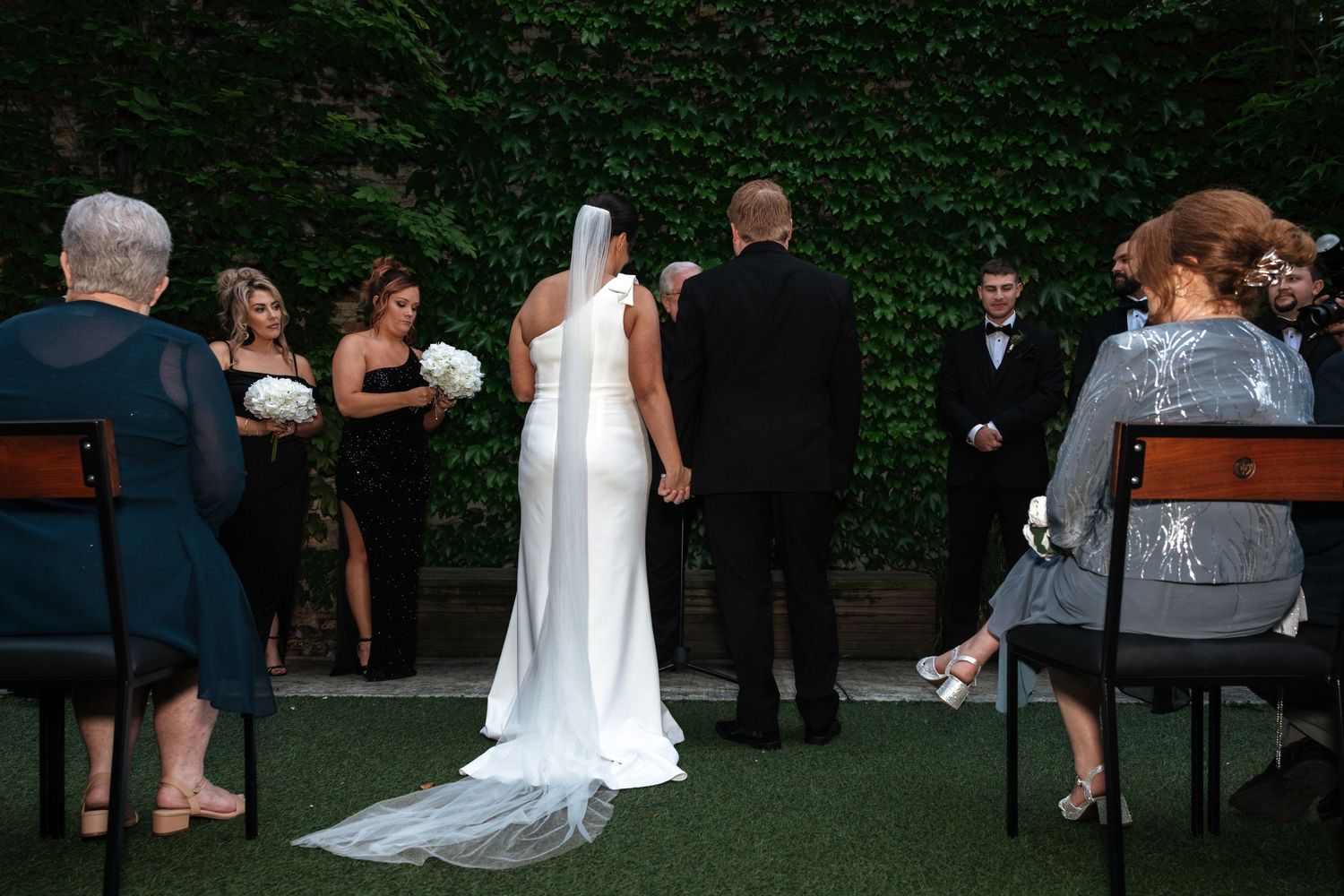 Bride and groom stand at the altar during an outdoor wedding ceremony with bridesmaids and guests.