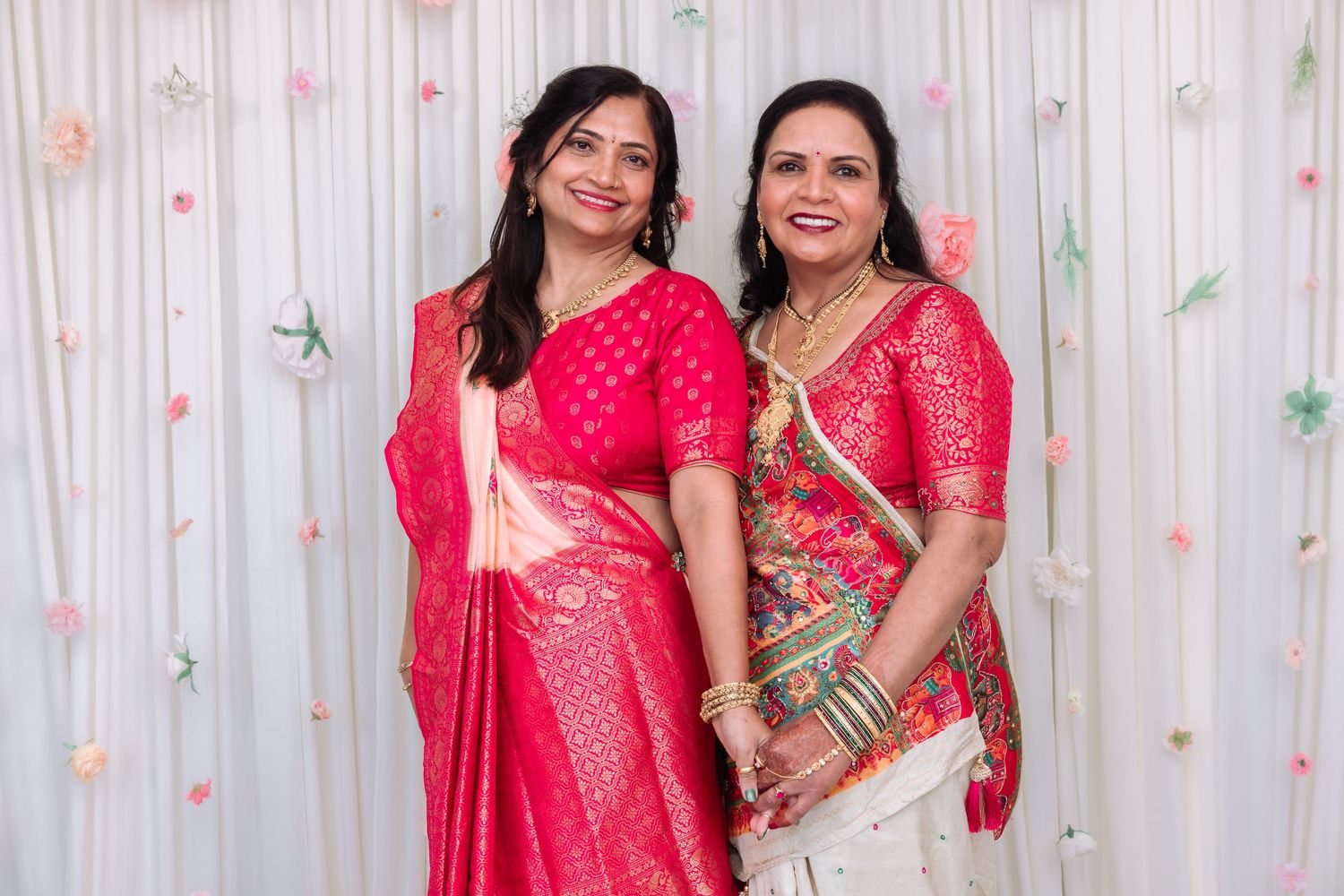 Two Indian women smiling in vibrant pink sarees at a festive celebration.
