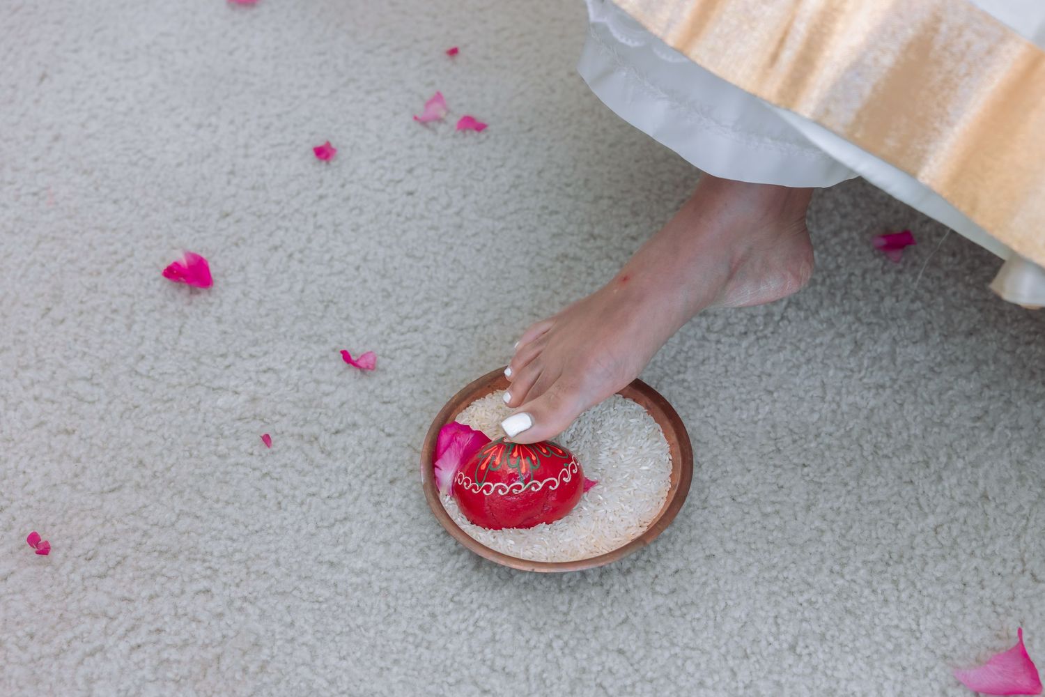 Bride's foot dips into bowl of milk and rose petals during traditional Hindu wedding ritual.