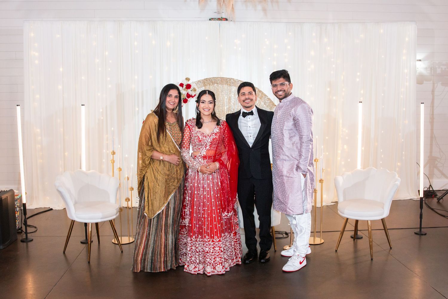 Four guests in traditional and formal attire posing at elegant Indian wedding reception venue.