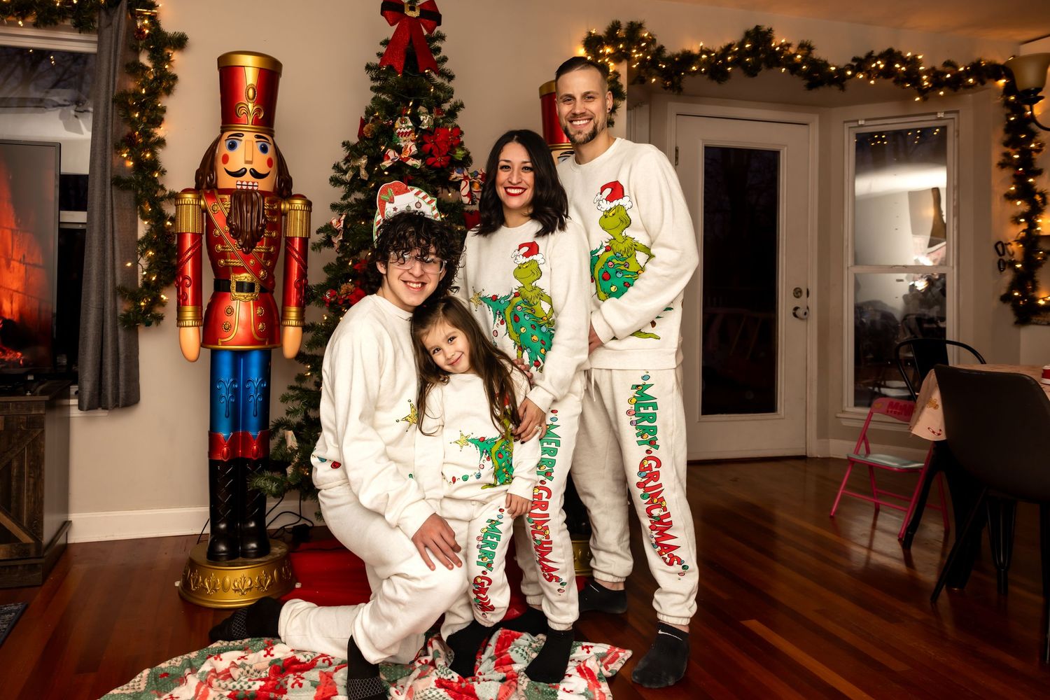 Family of four in matching Grinch Christmas pajamas posing by decorated tree.
