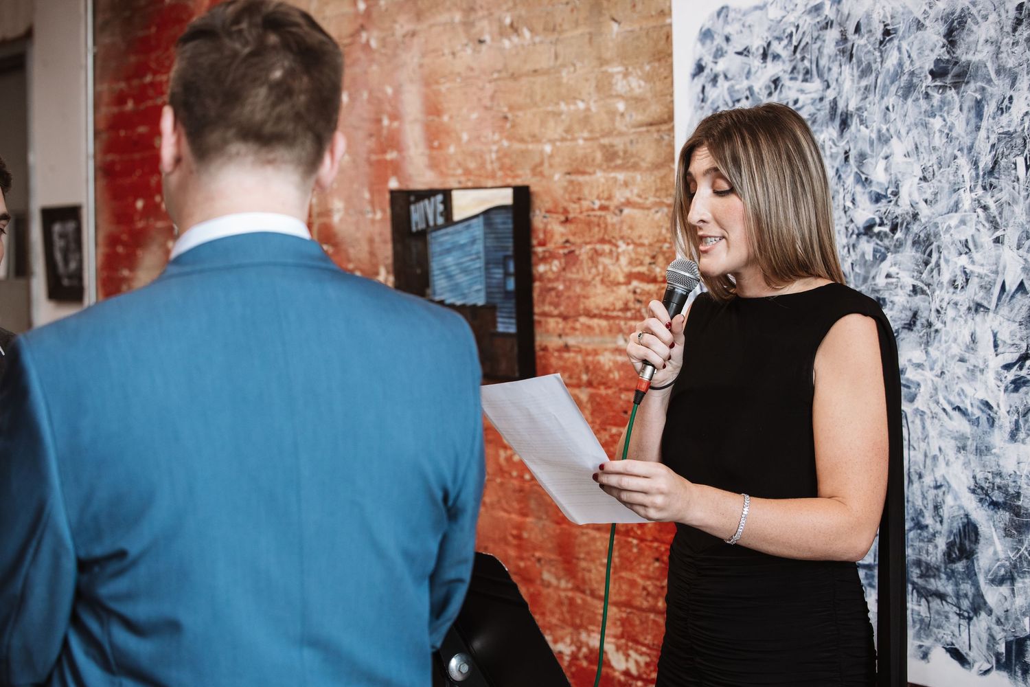Woman in black dress speaks into microphone at a wedding reception event.