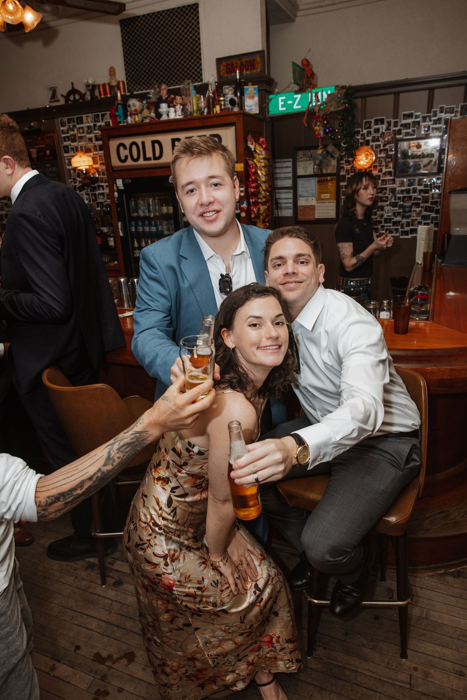 Three friends smile and raise drinks together at a vintage bar during a celebration.
