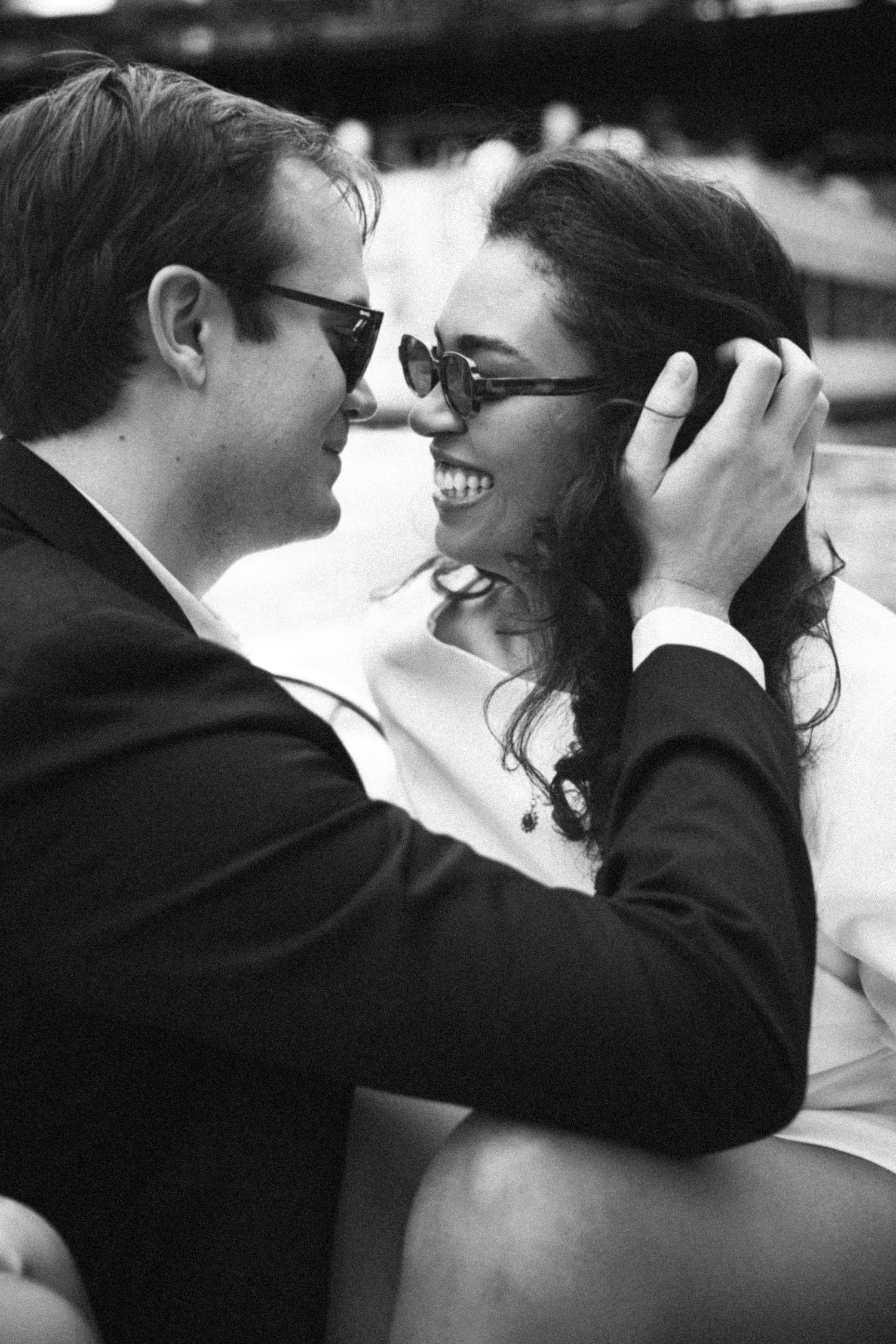 Black and white photo of laughing couple in sunglasses sharing a romantic moment during engagement session.