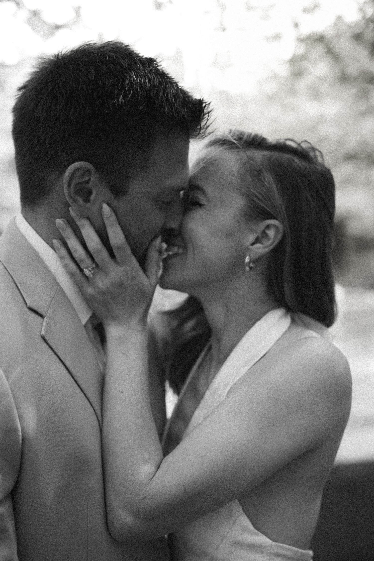 Black and white photo of smiling bride and groom sharing a romantic almost-kiss outdoors.