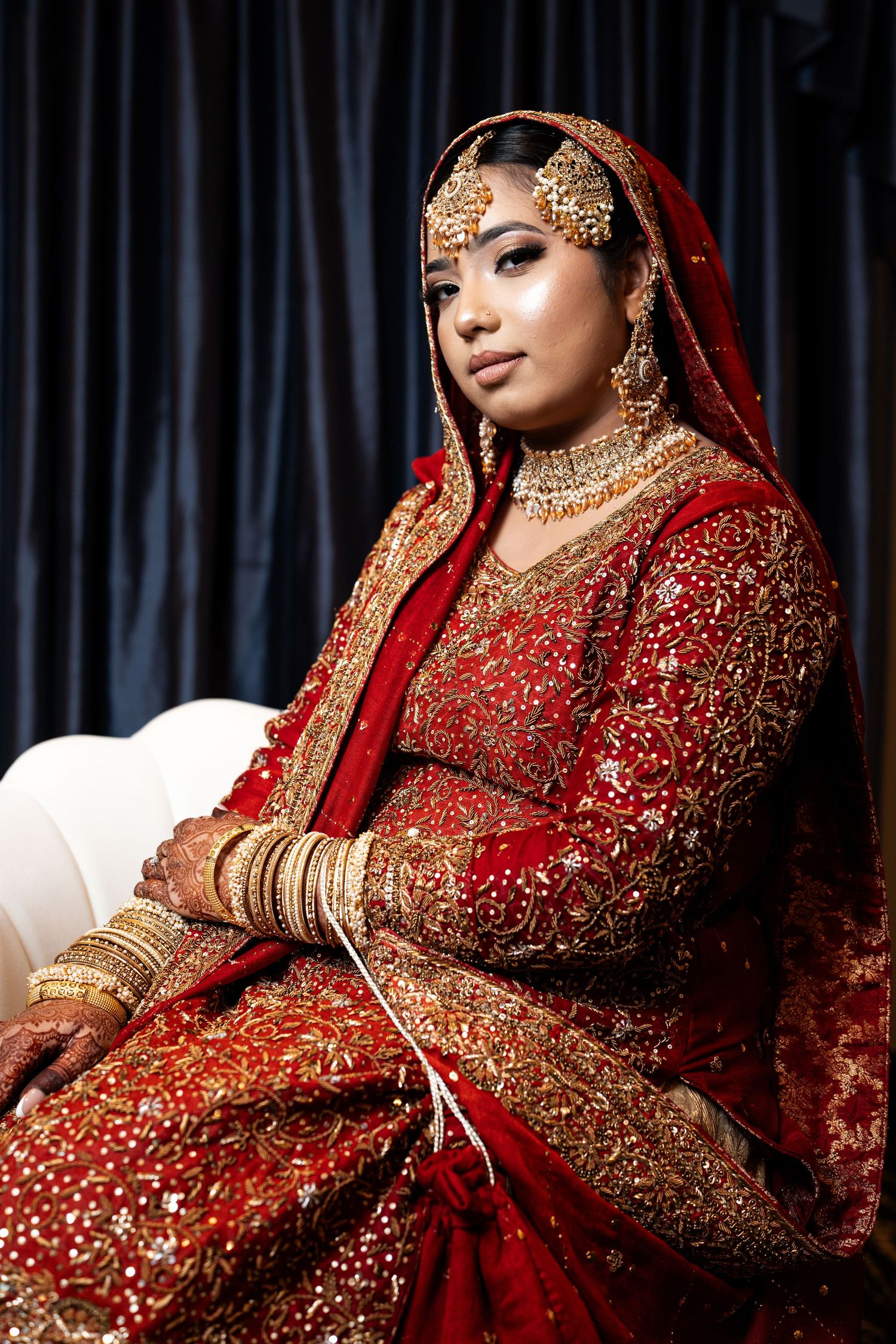 Bride in elaborate red and gold South Asian bridal lehenga with traditional jewelry.