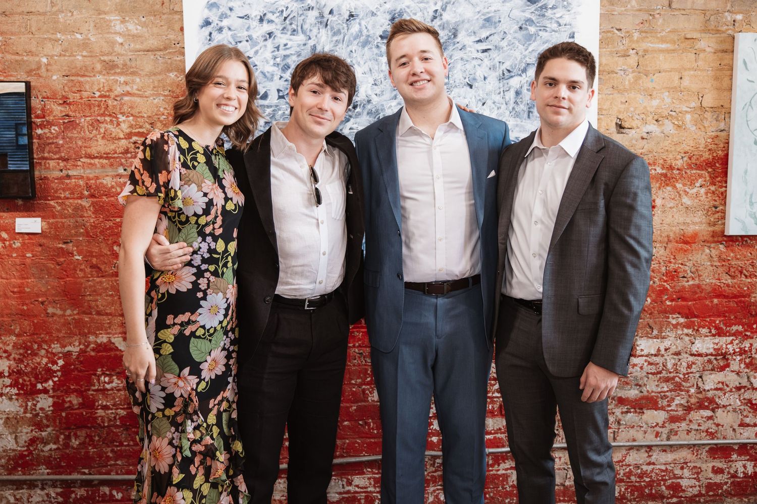 Four guests dressed in smart casual attire smile together at an art gallery reception event.