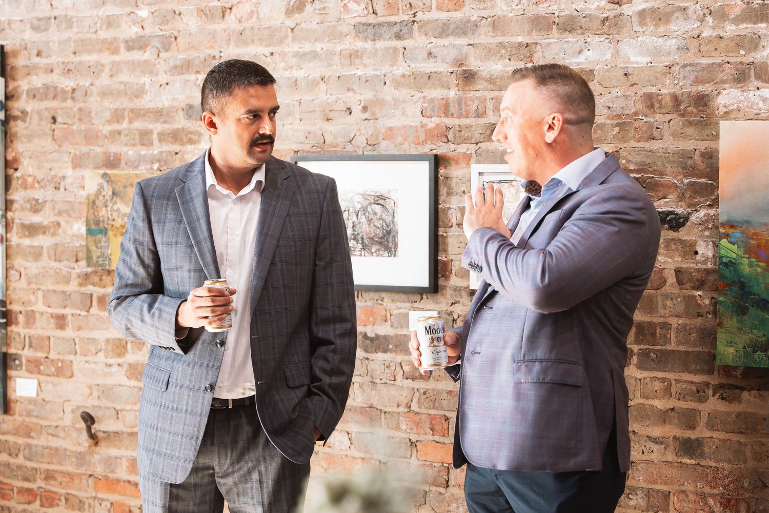 Two men in suits having a conversation at an upscale networking event with brick wall backdrop.