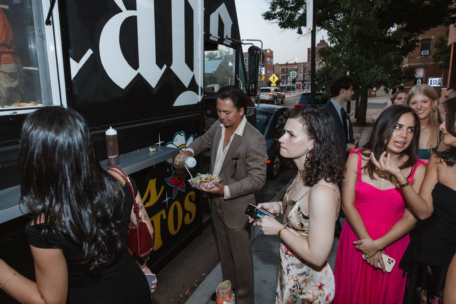 Wedding guests lining up at a food truck during an outdoor evening reception celebration.