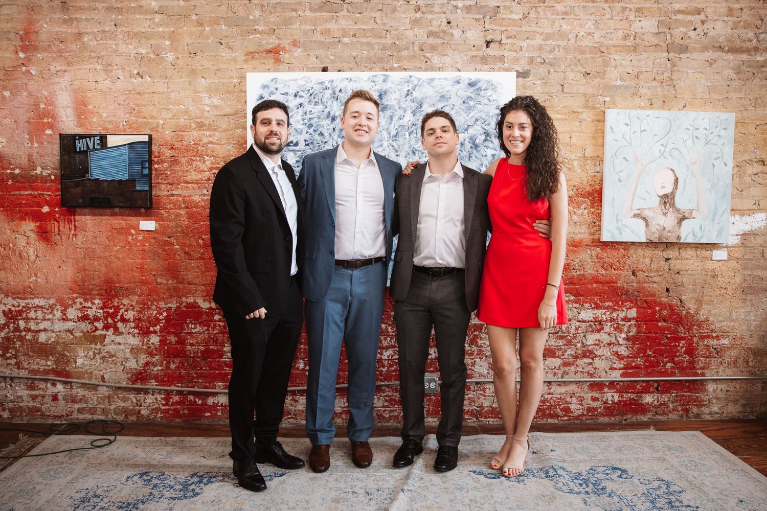 Four colleagues posing in front of artwork at a professional networking event in a gallery.