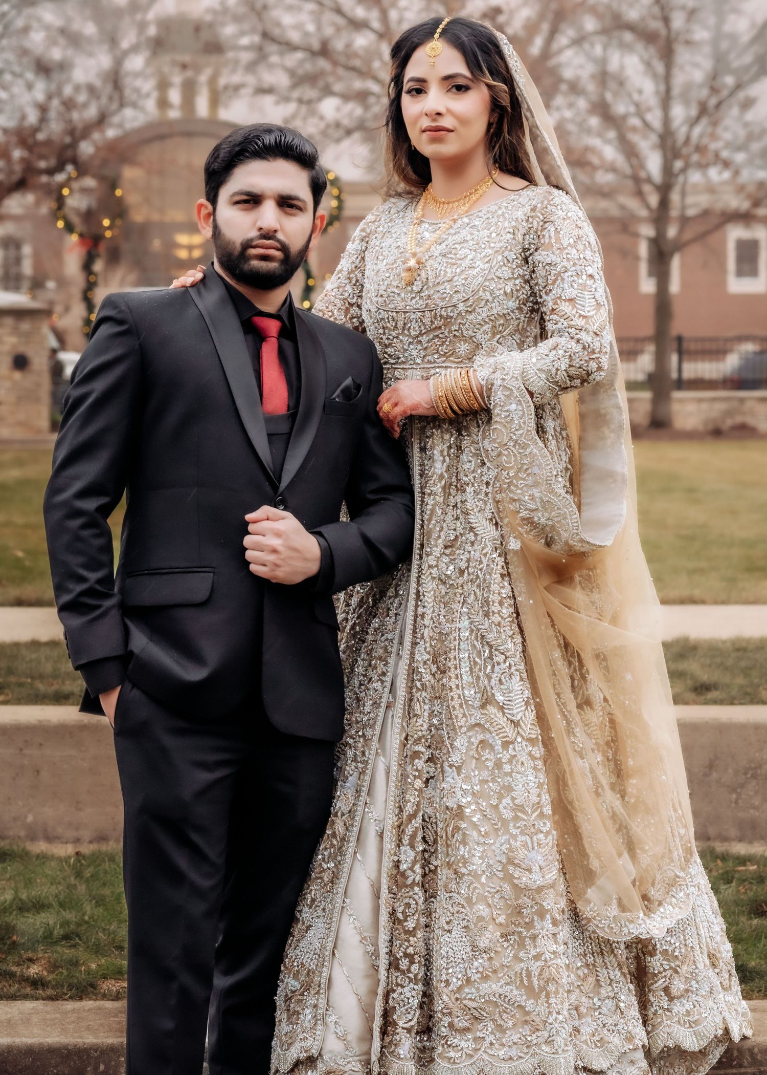 South Asian bride and groom pose formally outdoors, bride wearing stunning silver-gold embroidered bridal lehenga.